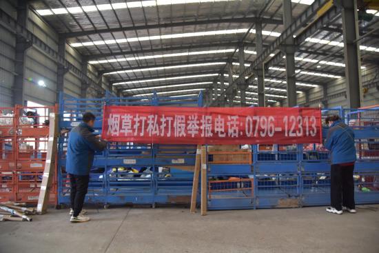 圖為執(zhí)法人員在物流園區(qū)懸掛卷煙打私打假宣傳橫幅